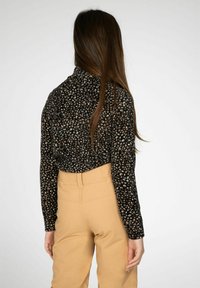 Langsleeve, getailleerde top in het zwart met een luipaardprint, gecombineerd met beige hoge taille broek. Zachte stof, gestructureerde afwerking.