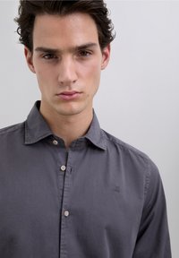 Grijs overhemd met knopen van lichtgewicht stof, voorzien van een kraag, knoopsluiting aan de voorkant en een klein logo op de linkerborst.