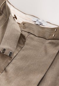 Pantaloni in tessuto marrone con sottili righe a spillo. Presentano una cintura liscia, chiusura lampo e ganci in metallo per una chiusura sicura. Interno foderato.