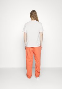 T-shirt en coton blanc et pantalon orange à jambes larges. Le t-shirt a un col rond et des manches courtes ; le pantalon est légèrement froncé aux chevilles.