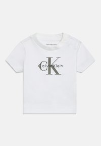 Biała bawełniana koszulka dla niemowląt z krótkimi rękawami, okrągłym dekoltem, zapięciem na napy z boku oraz dużym szarym logo "Calvin Klein" nadrukowanym z przodu.