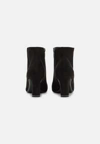 Botines de ante negro con tacón cuadrado, que cuentan con un cierre lateral de cremallera y una textura suave, diseñados para ajustarse cómodamente alrededor del tobillo.