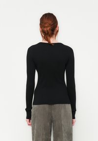 Haut à manches longues noir avec un design ajusté, texture côtelée et encolure arrondie, accompagné de pantalons en velours côtelé gris clair.