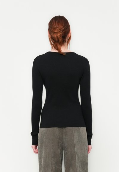 Haut à manches longues noir avec un design ajusté, texture côtelée et encolure arrondie, accompagné de pantalons en velours côtelé gris clair.