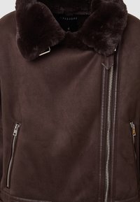 Giubbotto scamosciato marrone scuro con colletto in pelliccia morbida e chiusura con zip argentata asimmetrica, con tasche laterali con zip.