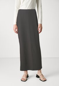 Maxi rok van donkergrijs ribstof, met een rechte snit en een elastische tailleband. Gepaard met lichtgekleurde sandalen met bandjes.