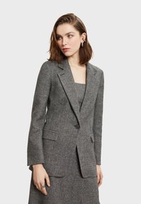Sivý herringbone blazer s priliehavým strihom, s klopami, dvoma prednými vreckami a jedným gombíkovým zapínaním. Hladká textúra, všestranný dizajn.
