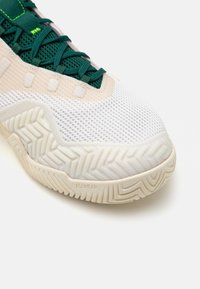 Hvide sportsko med mesh-overdel, grønne detaljer og tekstureret sål. Har en gummisål med fiskebensmønster og polstret mellemsål.