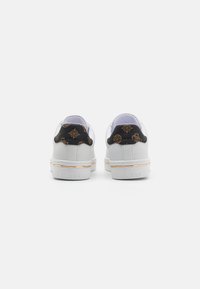 White sneakers with a textured black heel, featuring brown logo accents and a gold trim at the sole. Simple, low-profile design.