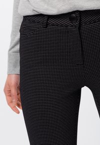 Pantalones negros con un sutil diseño de cuadros, de textura suave, con cierre de botón en la parte delantera y bolsillos estándar.