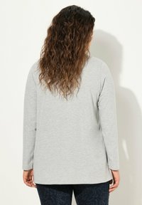 Graues langärmeliges T-Shirt aus weichem Stoff, mit lockerer Passform. Der Rücken hat einen abgerundeten Saum, ohne sichtbare Muster oder Details.