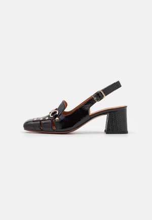 Black patent leather slingback shoe with block heel, buckle strap, cutout details, and silver buckle embellishment on front.