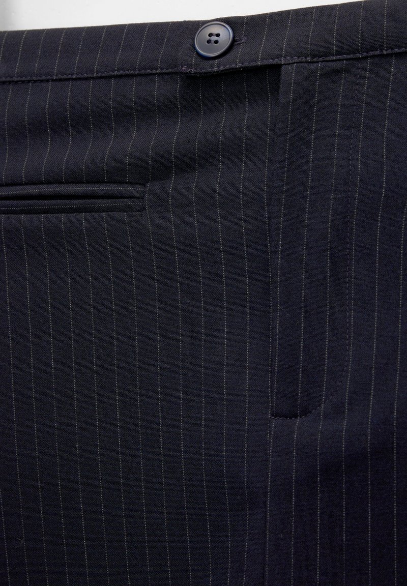 Le tissu à rayures marines présente une texture lisse, une fermeture à bouton proéminente et des poches latérales. De fines lignes verticales créent un motif classique.