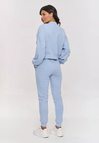 Jasnoniebieski, krótki sweatshirt i dopasowane joggery wykonane z miękkiego materiału. Posiadają ściągacze na rękawach i luźny krój, zestawione z białymi trampkami.