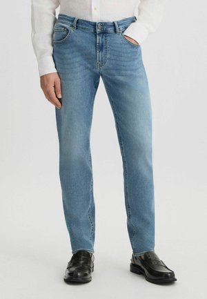 Jeans de mezclilla azul claro con corte recto, diseño de cinco bolsillos y detalles de costura sutiles, combinados con zapatos de cuero negros.