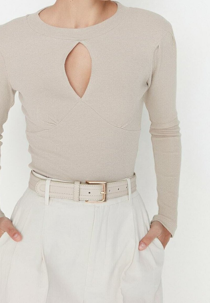 Haut beige côtelé à manches longues avec découpe en trou de serrure à l'avant, associé à un pantalon blanc taille haute et une ceinture beige assortie avec une boucle dorée.