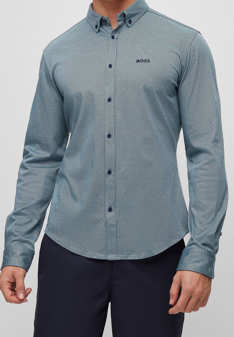 Langärmeliges Hemd mit Knopfleiste in hellem Türkis mit strukturiertem Muster. Verfügt über einen spitzen Kragen und dunkle Knöpfe. Kleines Logo auf der Brust.