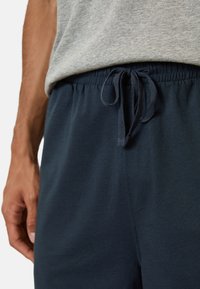 Námořnické modré tepláky s elastickým pasem, nastavitelnej šnúrkou a měkkou tkaninou, částečně viditelné pod šedým tričkom.