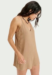 Vestido sin mangas de color tostado con un diseño de escote en V, hecho de tela texturizada, con tirantes finos y un corte holgado, que llega hasta la mitad del muslo.