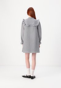 Abito grigio con scollo arricciato e maniche a sbuffo, caratterizzato da un motivo testurizzato. Indossato con ballerine nere e calze bianche al ginocchio.