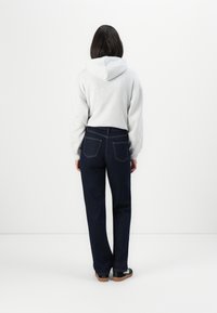 Grå hette-tröja, marinblå jeans och svarta skor. Jeansens har två bakfickor med sömnadsdetaljer.