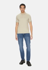 Polo shirt beige chiaro con colletto, maniche corte e tre bottoni. Indossato con jeans in denim blu e scarpe chunky nere.