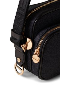 Sac bandoulière noir texturé avec quincaillerie dorée, comportant deux compartiments zippés et une bandoulière réglable à motif. Accents en cuir lisse.