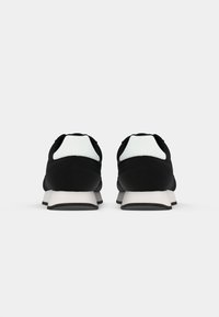 Black athletic shoes with a textured upper, white accents on the heel, and a contrasting gray sole design. Rounded toe shape.