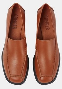 Des chaussures en cuir marron à enfiler avec une semelle plate noire, présentant des détails cousus et le nom de la marque "Camper" embossé à l'intérieur.