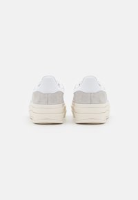 White and grey sneakers featuring a suede upper, layered midsole, and textured detailing on the heel. Minimalist design with contrast colors.