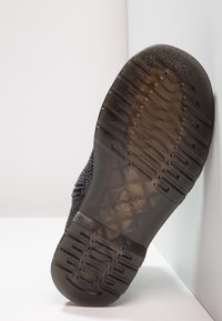 Suola di scarpa nera in gomma texturizzata, con un grip a motivo e un dettaglio logo distintivo. Il materiale sembra resistente e flessibile.