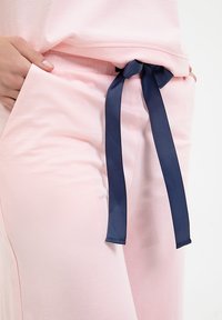 Jasnoróżowy zestaw odzieży domowej o gładkiej teksturze, z granatową kokardą w pasie i bocznymi kieszeniami. Prosty i wygodny design.