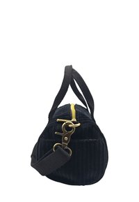 Sac en velours côtelé noir avec une fermeture éclair jaune, présentant une forme structurée, une surface texturée et une bandoulière détachable avec un clip en laiton.