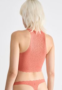 Koralfarvet bralette med bølget kant og racerback-design, parret med matchende tanga. Strækbart materiale med en glat tekstur.