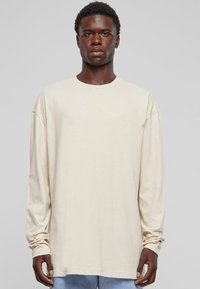 Tricou cu mânecă lungă, de culoare crem, într-o croială relaxată, cu gât rotund și umeri ușor lăsați, fabricat dintr-un amestec moale de bumbac.