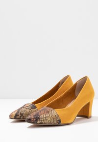 Décolleté gialli in suede con una punta a cappuccio a motivo testurizzato nelle tonalità di marrone e arancio. Tacco a blocco per stabilità e una struttura interna liscia.