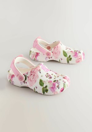Bloemenklompen in wit met roze accenten. Voorzien van een gestructureerde bovenkant bedrukt met bloemen, een achterstrap en ventilatiegaten.