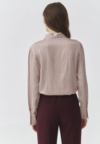 Langärmliges Hemd mit Knopfleiste in Hellbeige, mit ovalem Muster in Dunkelbraun. Glattes Material mit Kragen und geknöpften Ärmeln.
