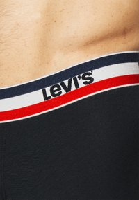 Črne bokserske hlače z belim, mornarsko modrim in rdečim prugastim pasom, na katerem je na sprednji strani viden logo "Levi's".