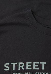 Czarna koszulka z krótkim rękawem wykonana z bawełny, z jasnozielonym napisem "STREET ORIGINAL SUPPLY" na przodzie. Gładka faktura.