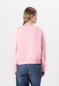 Svetlo roza sweatshirt z okroglim izrezom, spuščeni rameni in rebrastim robom. Ujemanje z modrimi kavbojkami visoke pasu. Teksturirana tkanina.