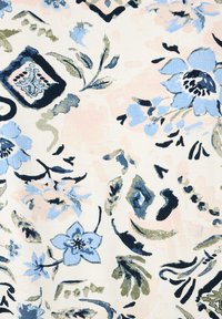 Bloemenstof met een lichtcrème achtergrond, versierd met blauwe en groene bloemen, zwarte accenten en abstracte vormen in een zachte textuur.