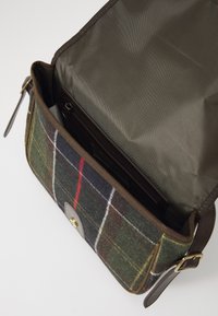 Groene en bruine tartan stof schoudertas met leren band, messingen gesp en een open flap die de bruine voering en ritsvak onthult.