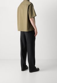 Kortærmet, olivengrøn skjorte med en afslappet pasform, kombineret med sorte bukser med vide ben og flade sorte sko. Glat tekstur, minimalistisk design.