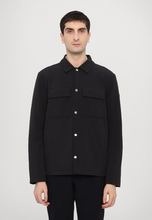 Black jacket made from smooth fabric, featuring a collared neckline, two front pockets, and snap button closure. Simple and streamlined design.