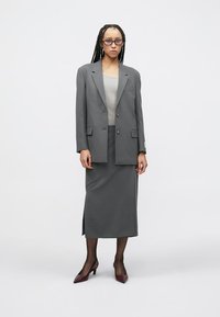 Γκρι σακάκι με δύο κουμπιά, φορεμένο πάνω από γκρι πλεκτό τοπ και αντιστοιχισμένη φούστα μήκους μέχρι τον αστράγαλο. Μπορντό μυτερά τακούνια ολοκληρώνουν το σύνολο.