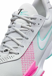 Baskets blanches de sport avec tige en maille, accents rose et turquoise, bout arrondi et système de laçage. Logo Nike bien visible sur la languette et sur le côté.