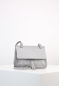 Šedá kožená kabelka přes rameno s klopou, nastavitelným popruhem a dvěma předními třásněmi. Texturovaný povrch s minimem kovových akcentů.