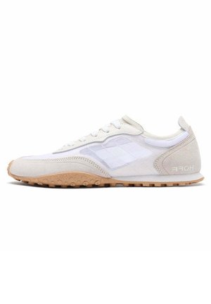 Zapatilla deportiva blanca con parte superior de malla, acentos de ante y suela de goma texturizada. Presenta un diseño simple de cordones y una marca en el talón.