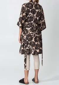 Blommig kimono i svart på en beige bakgrund, med vida ärmar, knytliv och ihop med beige capribyxor och svarta sandaler.